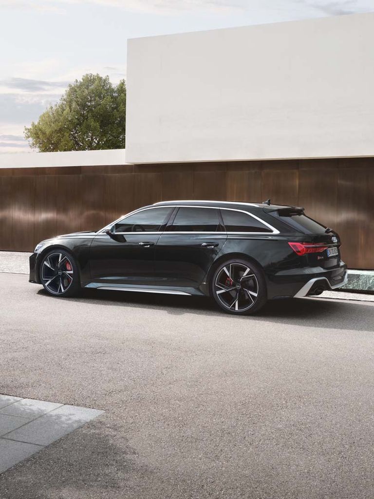 Side view of the RS 6 Avant in black in front of a modern house with a woman at the side